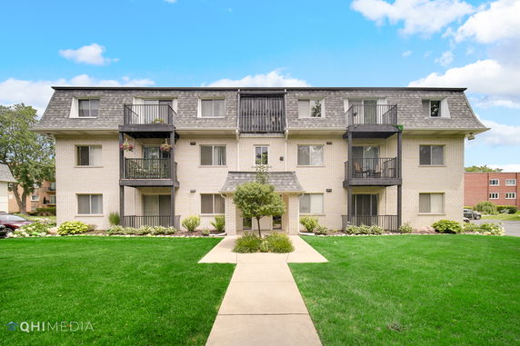 Front view of a three-story residential building with balconies and a shingled roof.