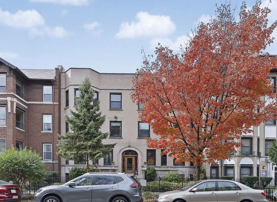 Front view of a multi-story residential building with autumn trees and parked cars.