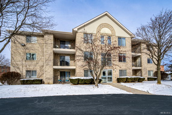 Front view of a three-story apartment building with a gable roof and multiple balconies.