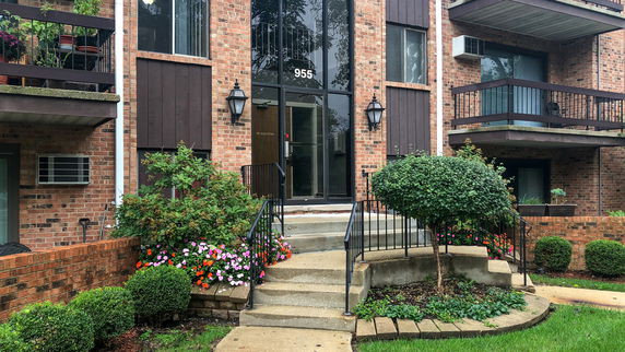 Front view of a brick multi-story building with balconies and entry steps.