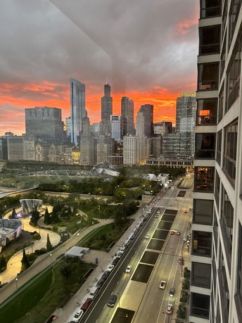 Panoramic view of a cityscape during sunset with tall buildings and a park visible.