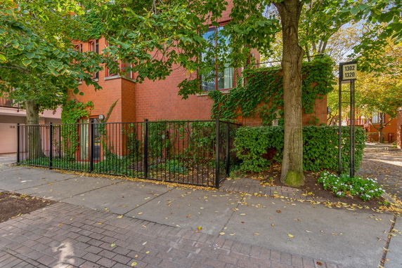 Front view of a two-story brick house with ivy and a black metal fence.