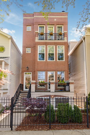 Front view of a multi-story brick building with balconies and potted plants.