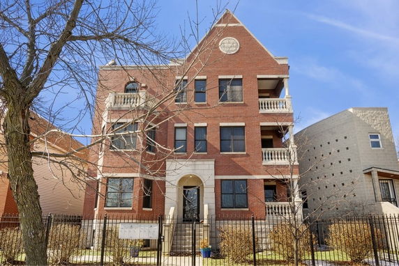 Front view of a three-story brick apartment building with balconies.