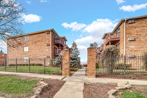 Front view of two brick apartment buildings with balconies and gated entrance.