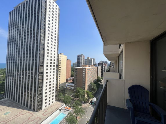 Panoramic view of a cityscape from a balcony with high-rise buildings and partially visible swimming pool below.