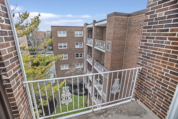 View from a balcony showing nearby brick residential buildings and surrounding trees.
