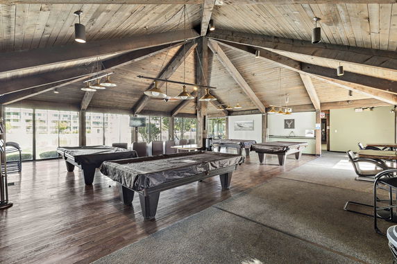 Interior view of a clubhouse with multiple billiard tables and wooden beams on the ceiling.