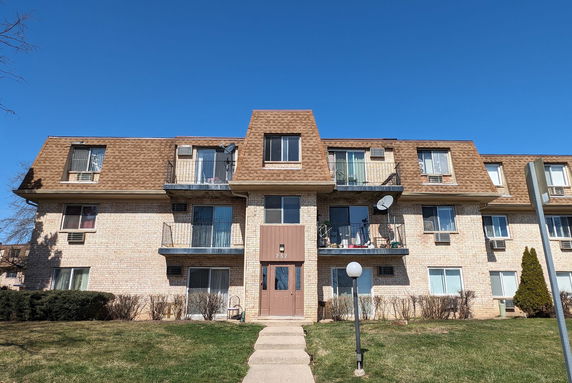 Front view of a three-story apartment building with balconies and brown roof.