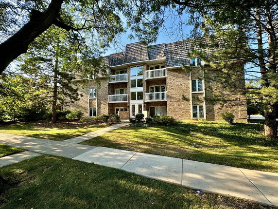 Front view of a three-story brick apartment building with balconies.