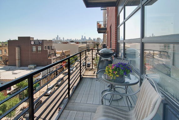 View of cityscape from a balcony with seating and a grill.