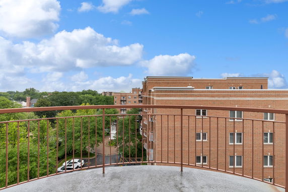 View from a balcony overlooking trees and brick buildings under a blue sky.