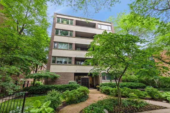 Front view of a multi-story apartment building with brick facade and surrounding trees.