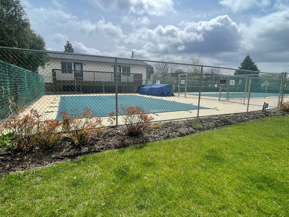 A fenced tennis court with a covered surface next to a residential building.