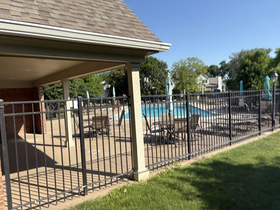 Outdoor swimming pool area with chairs and umbrellas, fenced enclosure.