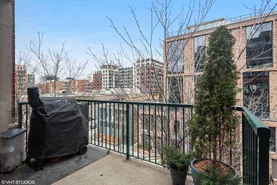 View of a balcony with a grill and potted plants, overlooking surrounding buildings.