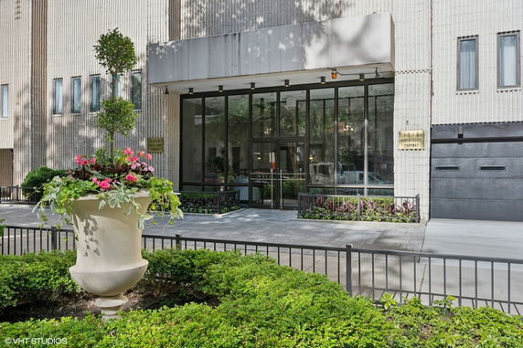 Front view of a building entrance with glass doors and windows, and decorative plants.