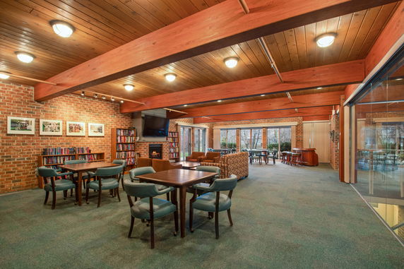 Indoor club house with wooden beams, tables, chairs, and bookshelves.