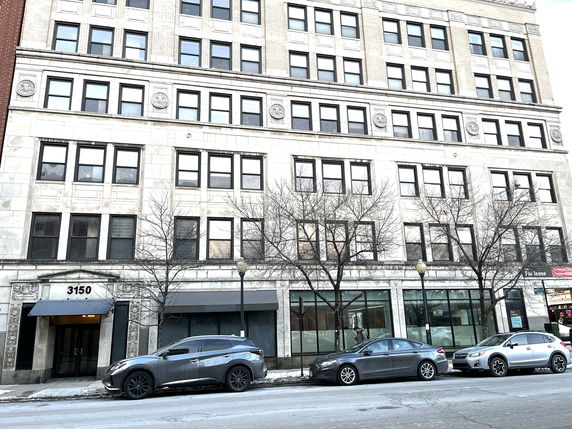 Front view of a multi-story building with large windows and street parking.