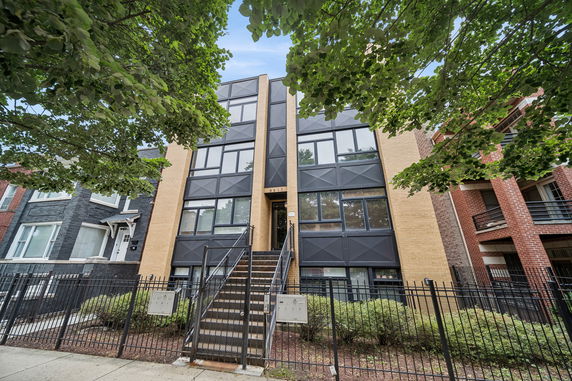 Front view of a modern multi-story building with a metal staircase and large windows.