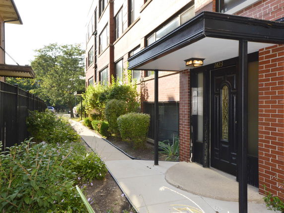 Front view of a multi-story brick apartment building with a covered entrance.