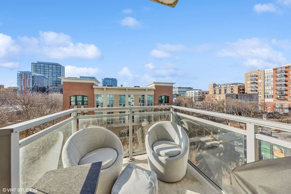Elevated view showcasing urban buildings and a clear sky from a balcony with two chairs.