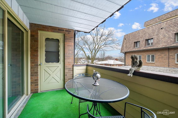 Balcony with a round table and chairs, overlooking rooftops and a tree, with a decorative figure on the railing.