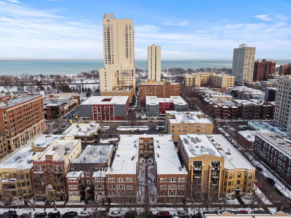 Panoramic view of a cityscape with mid-rise and high-rise buildings, seen from above. Snow covers the rooftops and grounds.