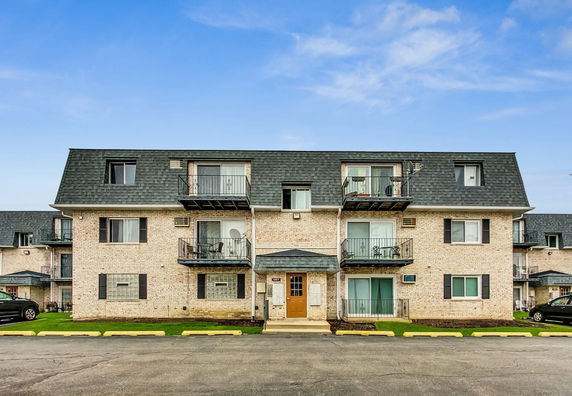 Front view of a three-story brick apartment building with balconies.