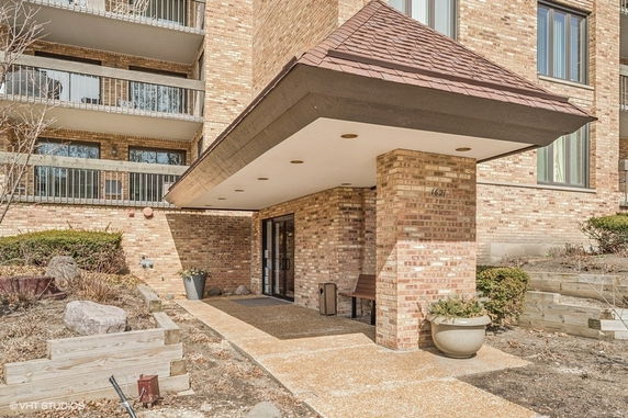 Front view of a brick building entrance with covered porch and multiple balconies.