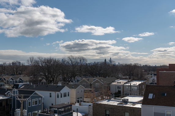 Panoramic view of rooftops and distant skyline with trees and clouds.