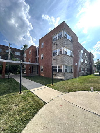 Front view of a multi-story brick building with several windows and a paved walkway.