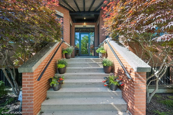 Front view of a brick building entrance with stairs and potted plants.