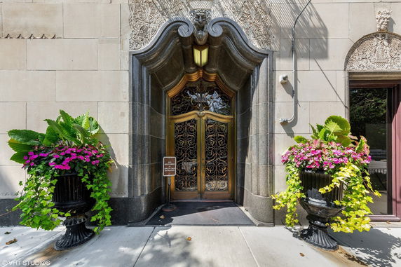 Entrance of a building with ornate metal doors, intricate stonework, and decorative planters.