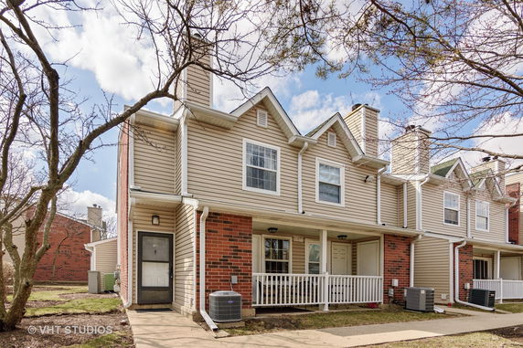 Front view of a two-story townhouse with a covered porch and brick accents.