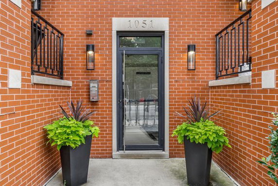 Front view of a brick building entrance with glass door and black metal railings.