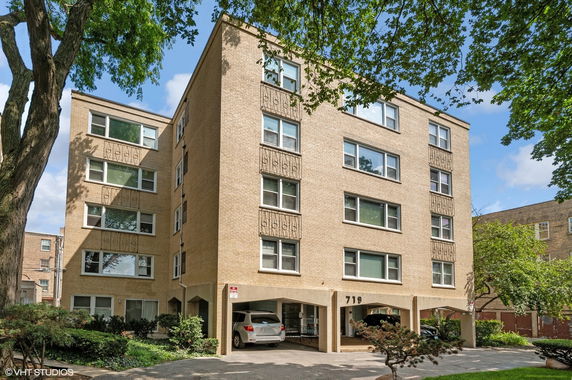 Front view of a multi-story apartment building with multiple windows and parking spaces underneath.