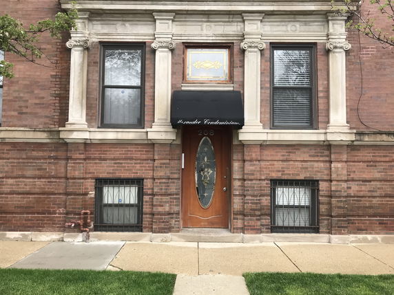 Front view of a brick building with decorative columns and a wooden door.