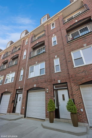 Front view of a multi-story brick townhouse with garage doors and balconies.