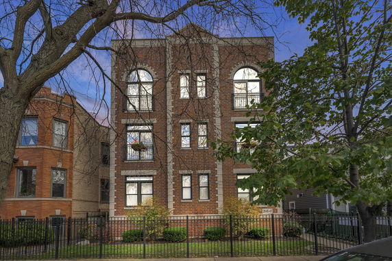 Front view of a multi-story brick building with arched windows and a fenced yard.