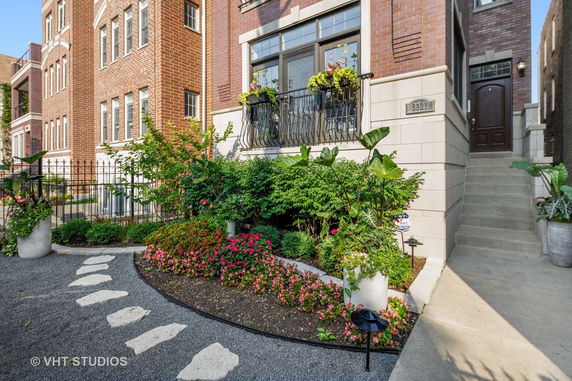 Front view of a multi-story brick residential building with decorative plants and a garden.
