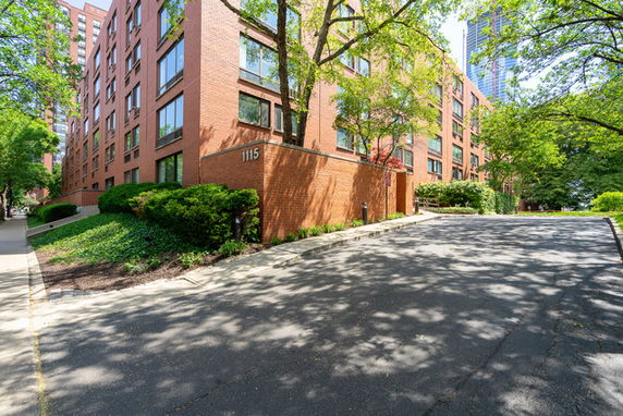 Front view of a brick multi-story apartment building with trees and sidewalks.