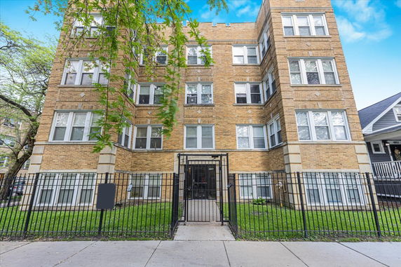 Front view of a multi-story brick building with a gated entrance.