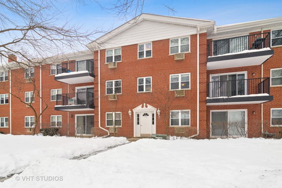 Front view of a three-story brick apartment building with balconies and a central entrance.
