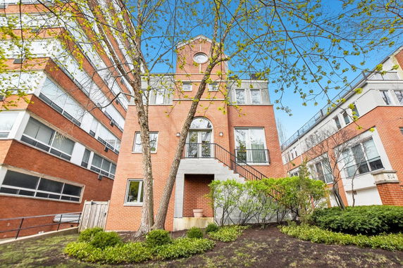 Front view of a brick multi-story building with a gable roof and entrance stairs.