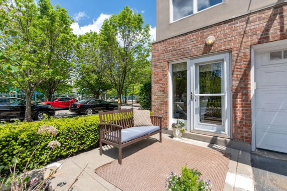Front view of a house with a brick facade and glass door, featuring a small bench and outdoor rug.