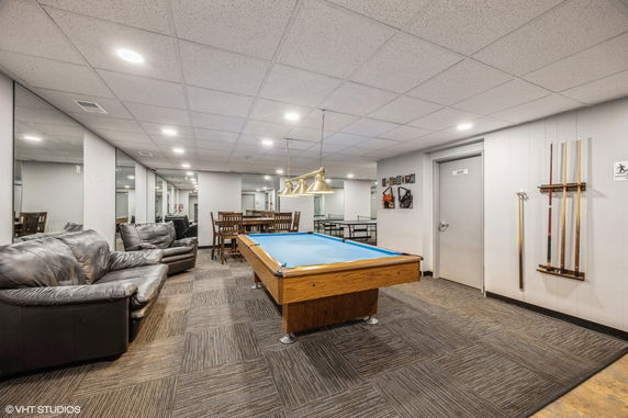 Interior view of a recreation room with a pool table, seating area, and dining table.