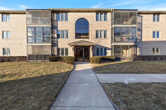Front view of a three-story residential building with brick facade and enclosed balconies.