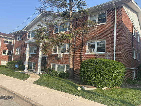 Front view of a three-story brick apartment building with white pillars at the entrance.