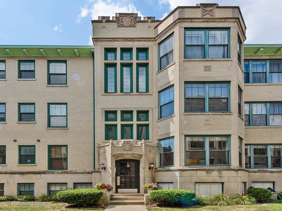 Front view of a multi-story building with decorative stone facade and green-framed windows.